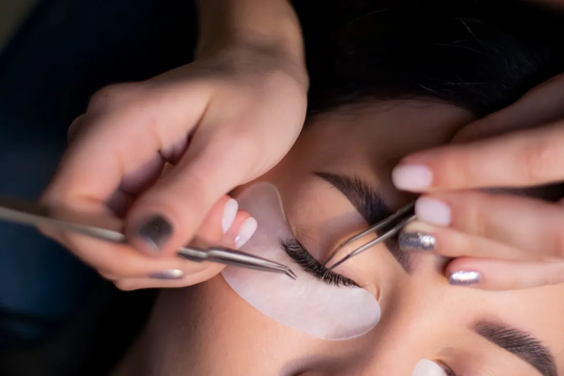 Isolating natural lashes with tweezers over protective under-eye patches